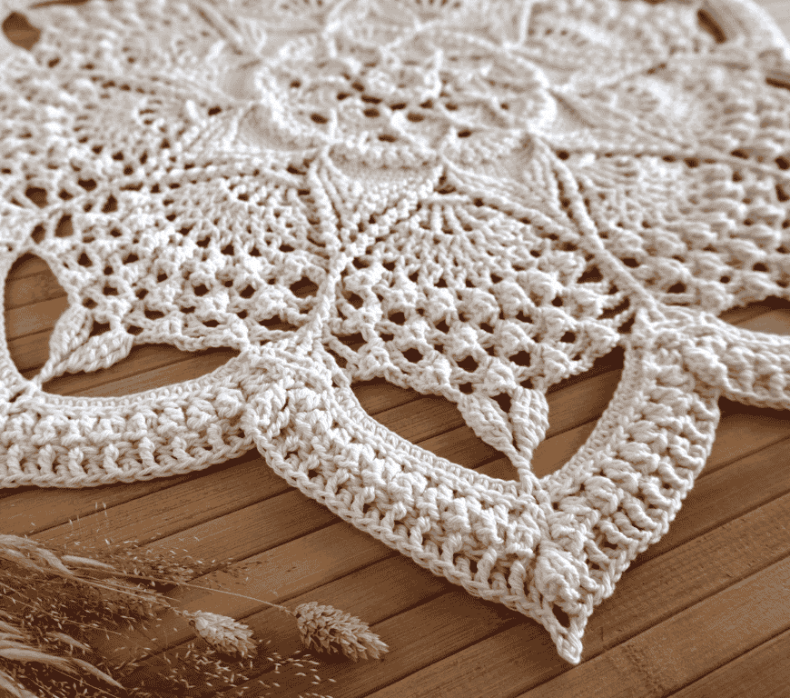 Mandala de crochet Lotus Quiet sobre una superficie de madera con un ramillete de flores secas.
